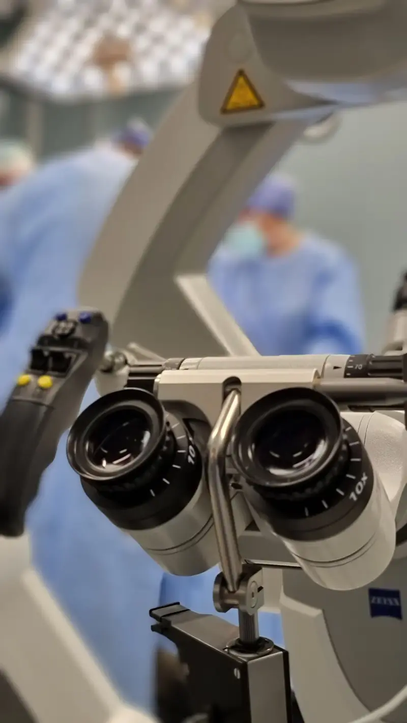 Surgical microscope in an operating room with a blurred surgical team behind it