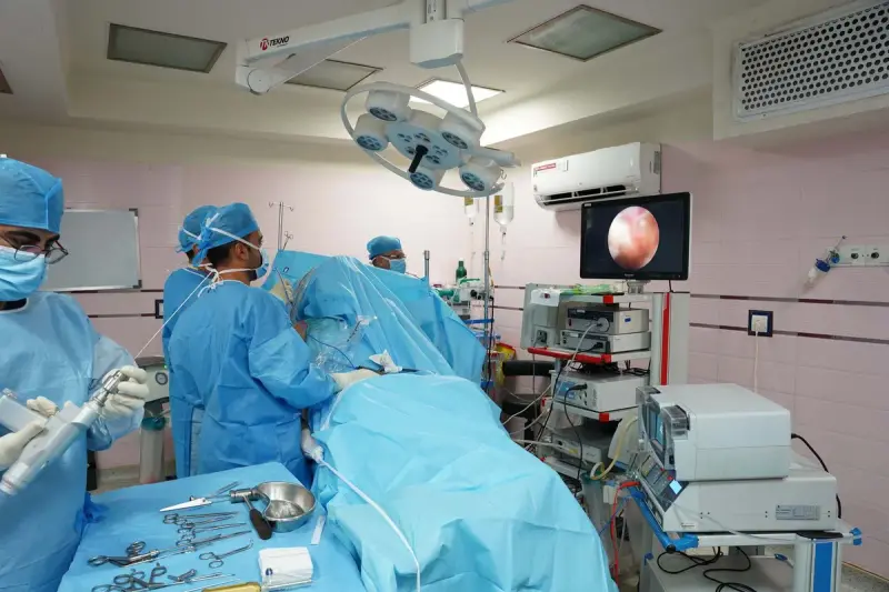 Surgical team in blue gowns during an endoscopic procedure, the scope image shown on a wall monitor