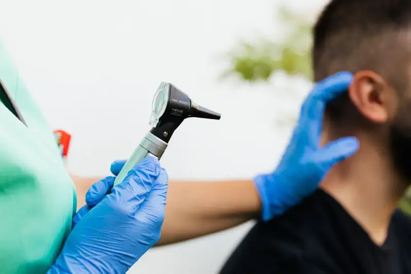 Gloved clinician holds an otoscope while steadying a patient's head before an ear exam
