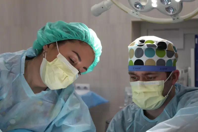 A woman surgeon and a male colleague in masks and caps focus on an operation
