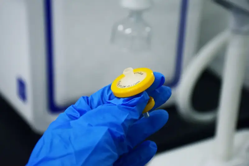 Blue-gloved hand holding a small syringe filter used to prepare samples for analysis