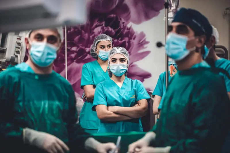 Surgeons in green gowns and nurses in teal scrubs watching a procedure in an operating room
