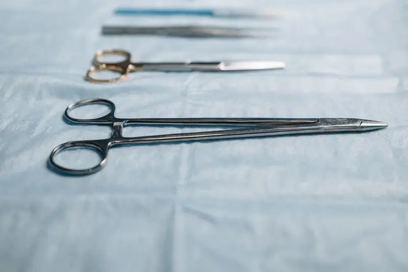 Steel needle holder and surgical scissors laid on a pale blue sterile drape
