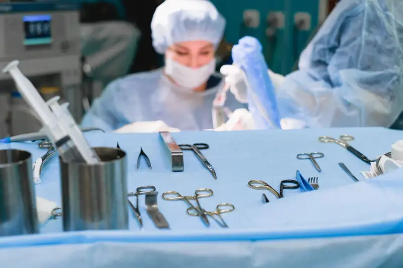 Clamps, forceps and scissors on an instrument table with a masked surgeon working behind it