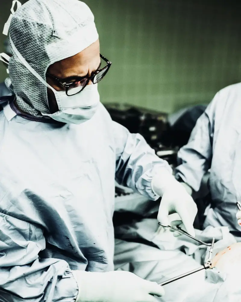 Surgeon in a cap, mask and glasses holding steel instruments during an operation