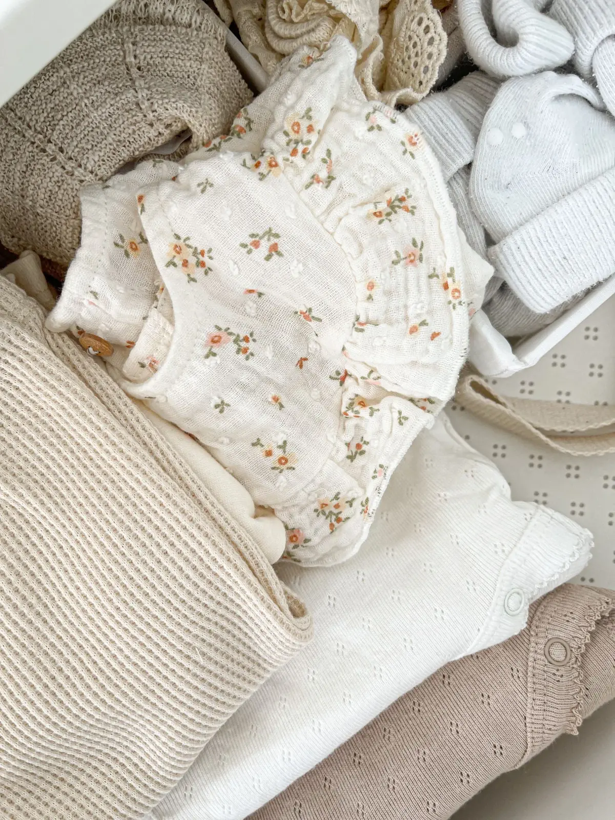 Neutral-colored baby garments arranged to show fabric and embroidered details