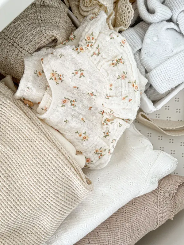 Neutral-colored baby garments arranged to show fabric and embroidered details