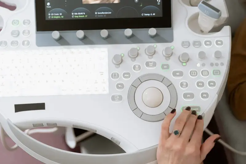 Hand on the trackball of an ultrasound console with knobs, keyboard and a docked probe