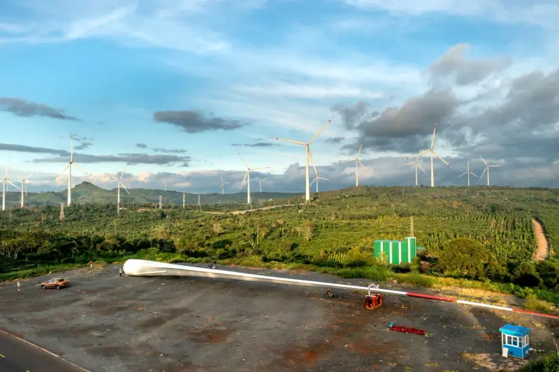 Wind farm with turbines, service equipment and green fields under a blue sky
