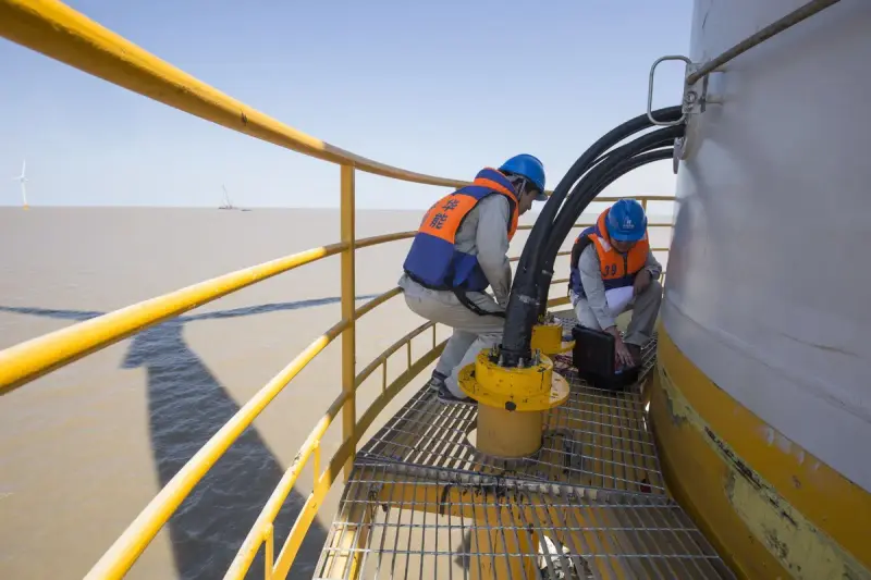 Technicians in harnesses and safety gear working on top of an offshore wind turbine