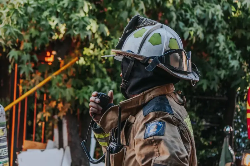Firefighter in full protective gear using a radio outdoors