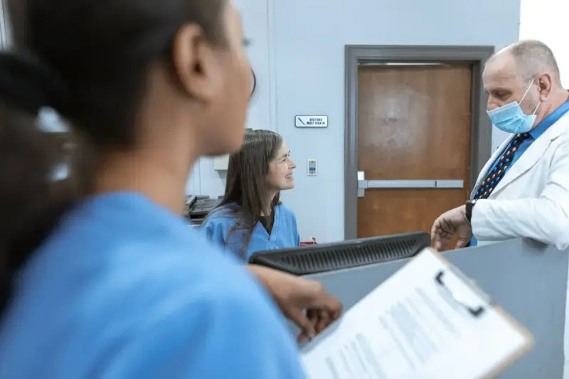 Clinicians conferring over a clipboard at a hospital reception desk