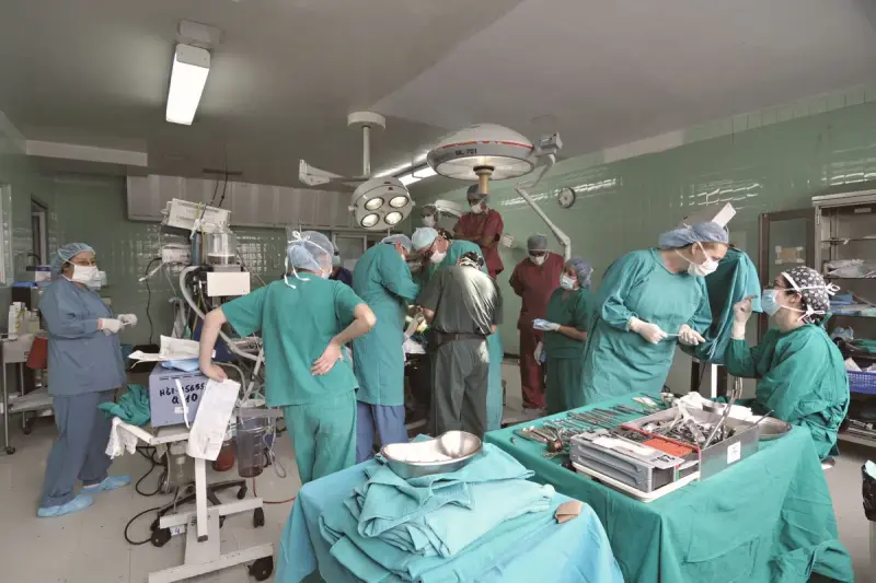 Full surgical team of women and men in scrubs working around an operating table and instrument trolley