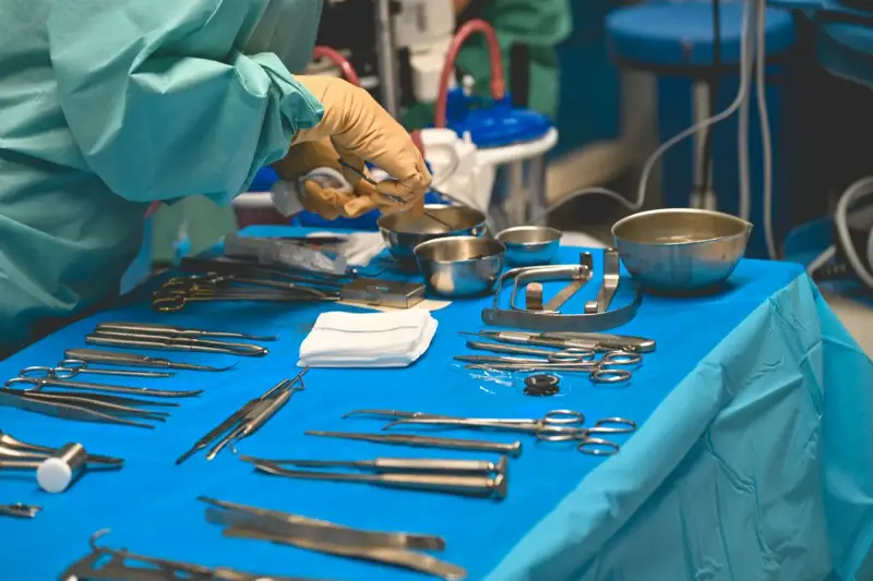 Scissors, clamps, retractors and steel bowls laid out on a blue sterile table