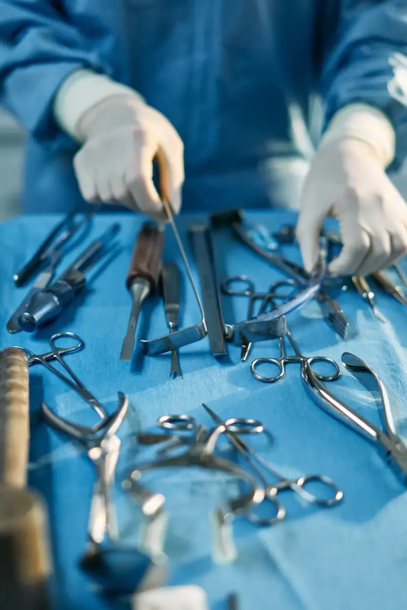 Gloved hands arranging retractors and forceps on a blue surgical drape