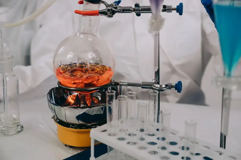 Round-bottom flask of orange liquid heating on a mantle beside a rack of test tubes