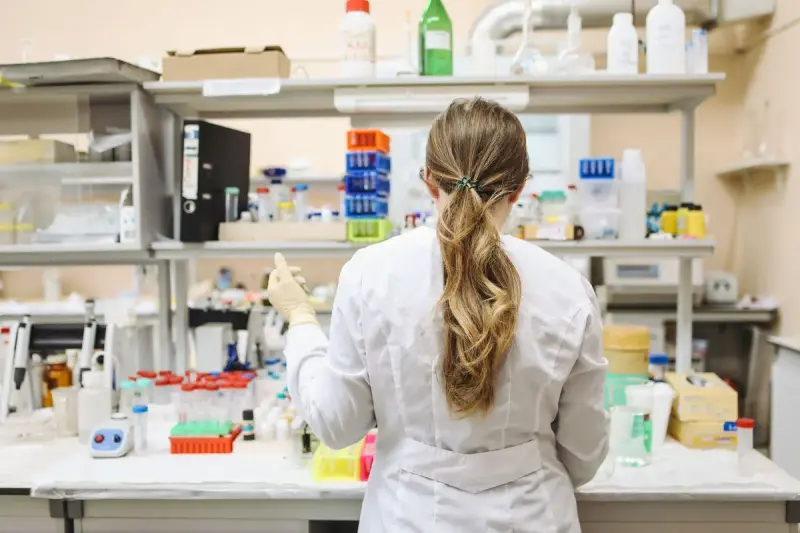 Female scientist in a lab coat and gloves working at a stocked laboratory bench