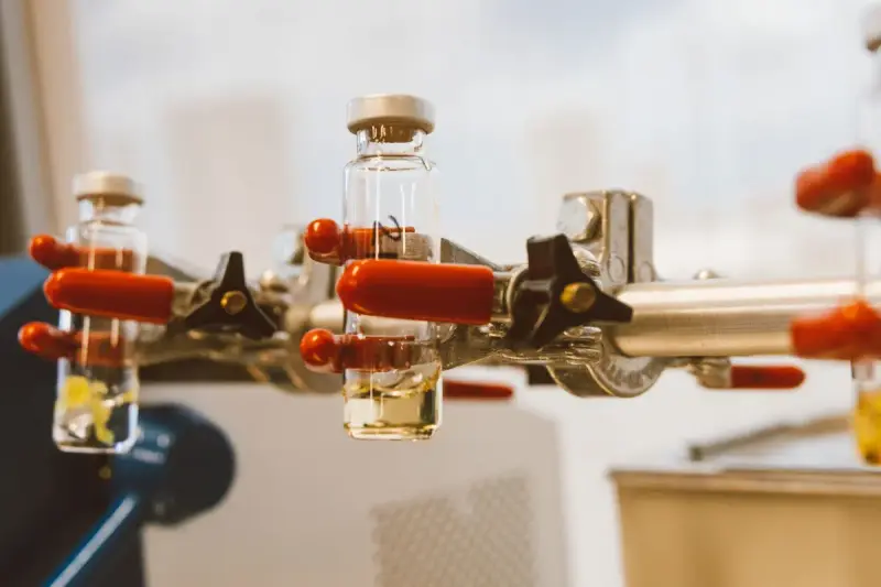 Laboratory glass vials held upright by a clamp with red handles