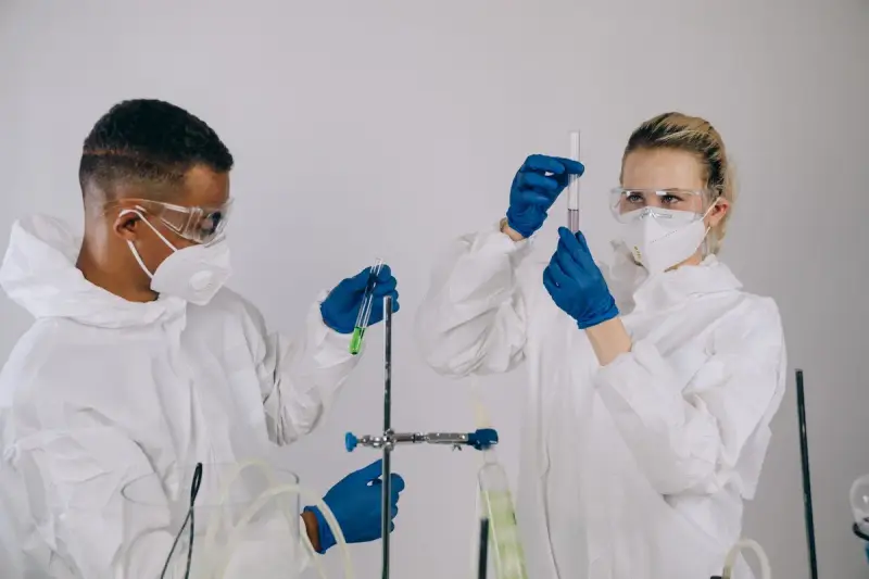 Two chemists in protective suits and goggles measuring liquid in a pipette