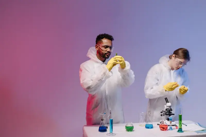 Two scientists in white protective suits working with test tubes and colored solutions