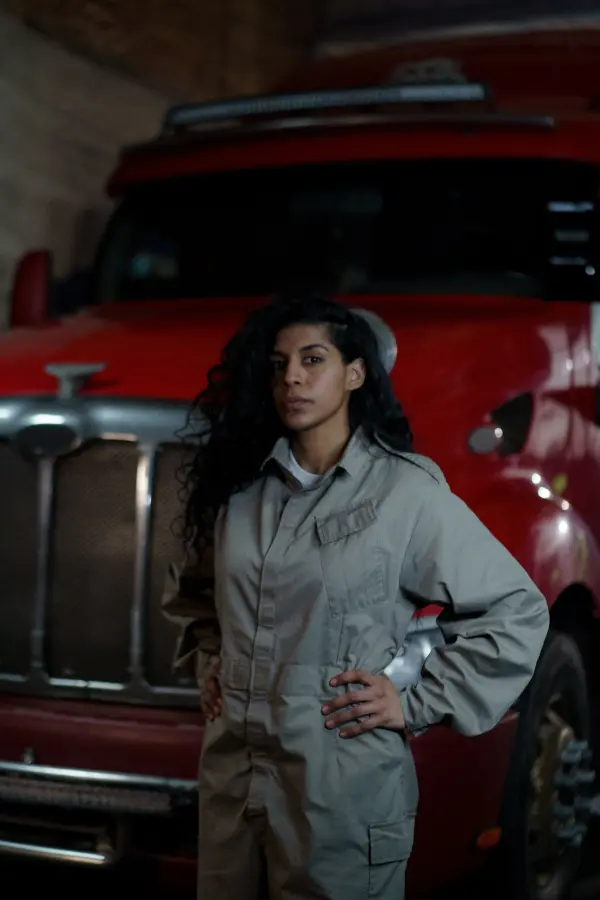 Woman in a gray work uniform beside a red truck indoors