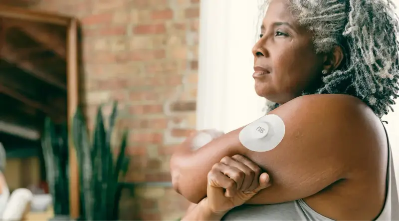 Woman with gray hair wearing a continuous glucose monitor sensor on her upper arm