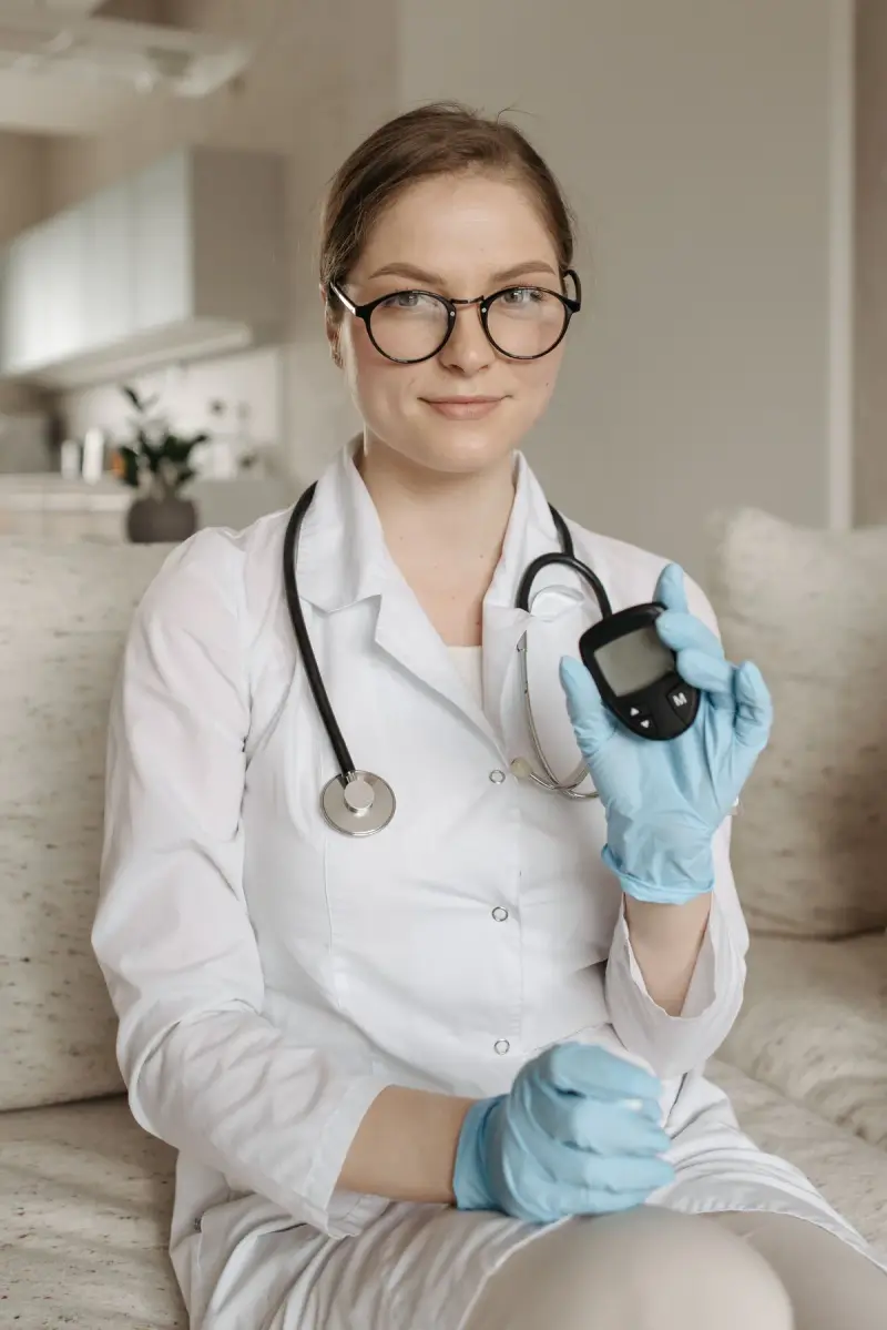 Female doctor in glasses and gloves holding up a blood glucose meter
