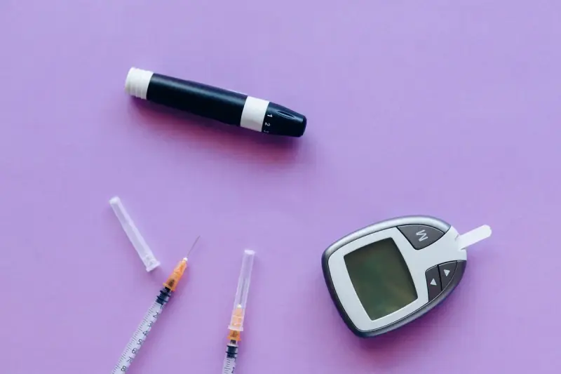 Glucose meter, lancing pen and insulin syringes laid out on a purple surface