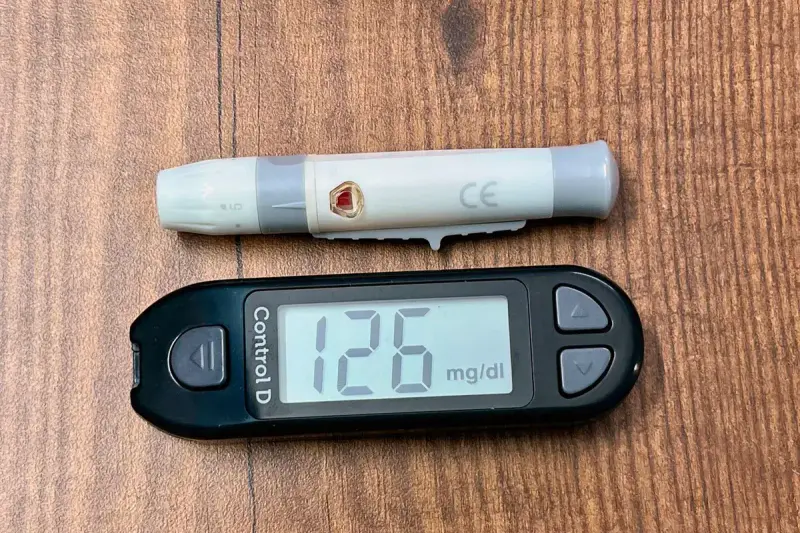 Digital glucose meter showing a reading of 126 mg/dL beside a lancing device