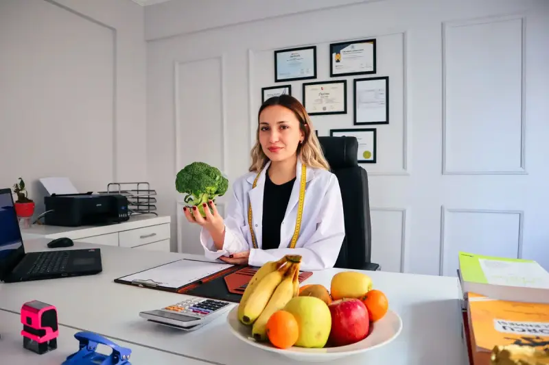 Nutritionist at her office desk holding broccoli beside a bowl of fruit