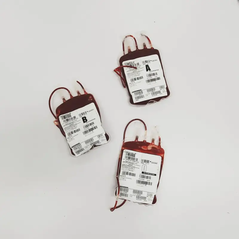 Three blood donation bags labelled by blood type on a white surface