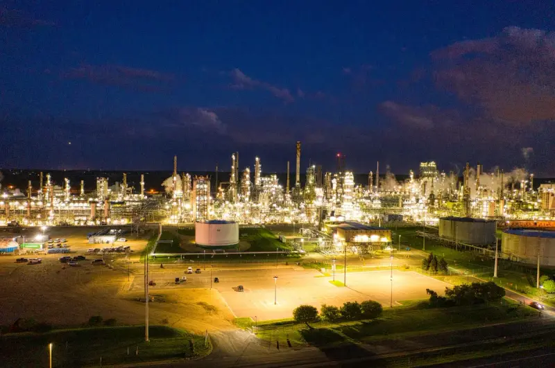 Aerial view of an oil refinery lit up at night beside a parking area