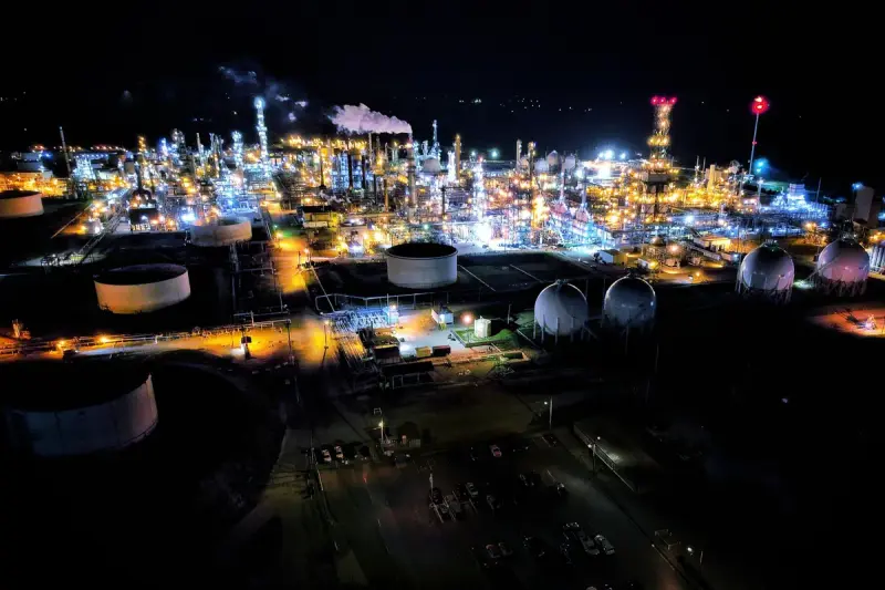 Aerial night view of a brightly lit refinery with storage tanks