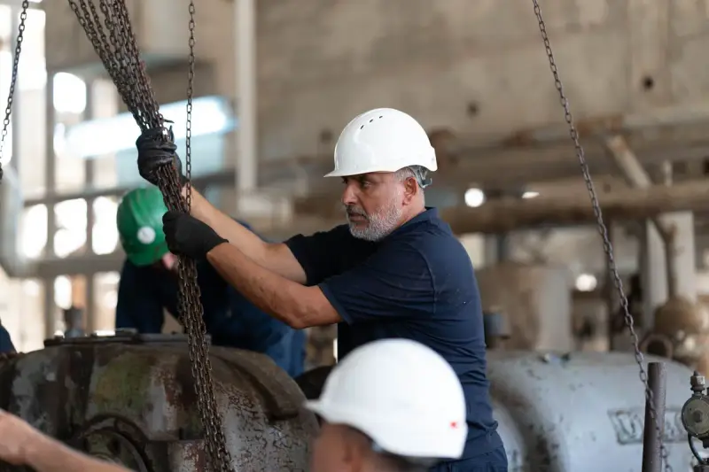 Plant technicians in hard hats rigging chains on heavy machinery