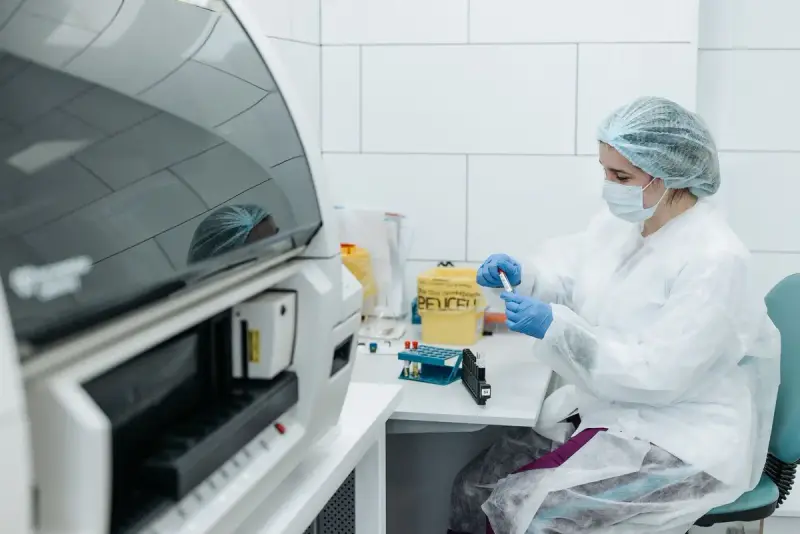 Scientist in protective gear holding up a labeled sample tube