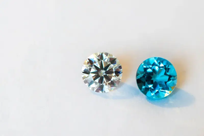 A round brilliant diamond beside a faceted blue gemstone on a white surface
