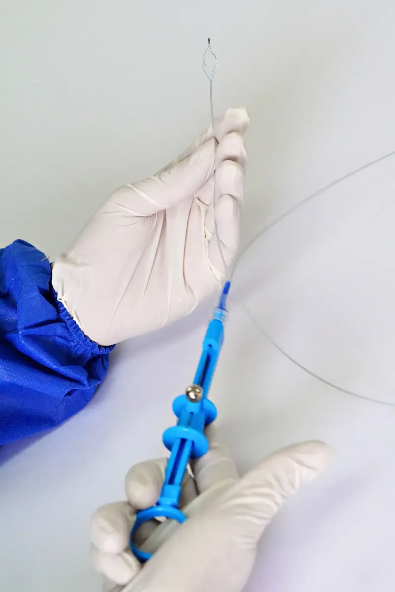 Gloved hands holding a thin catheter wire and its blue handle against a white background