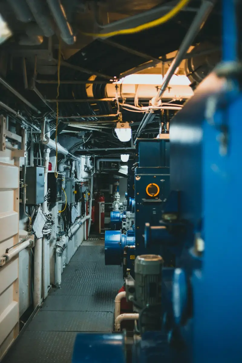 Mechanical corridor with blue pumps, motors and overhead pipes and cable trays