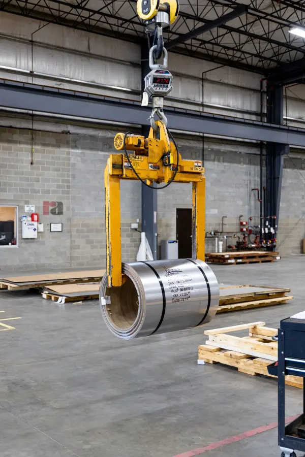 Metal coil suspended from lifting equipment inside an industrial facility