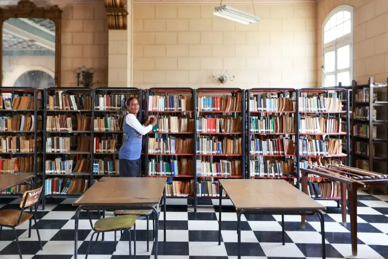 Librarian organizing books in a classic library with checkered flooring