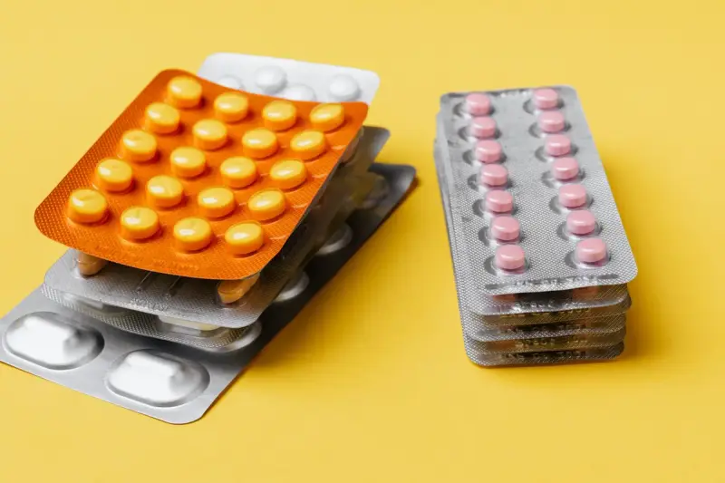 Stacks of orange and silver blister packs holding yellow and pink tablets on a yellow surface