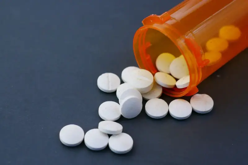 White tablets spilling from an orange prescription vial onto a dark gray surface