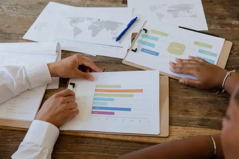 Hands on a wooden table covered with printed bar charts, maps and a flow diagram