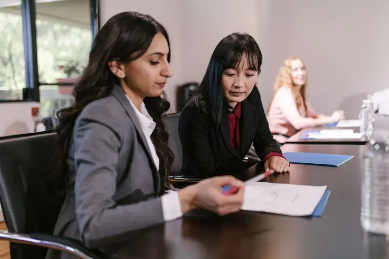 Two businesswomen reviewing a printed document together at a boardroom table