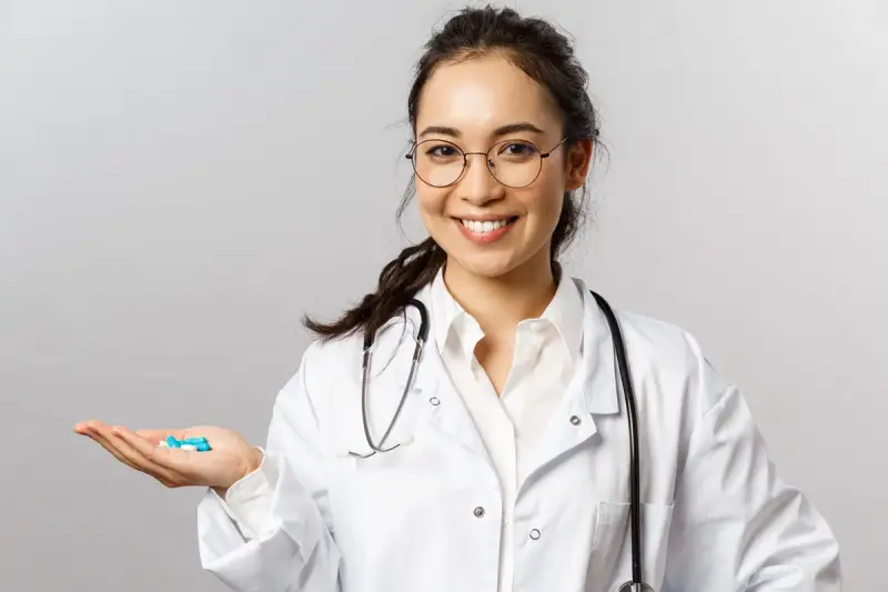 Smiling clinician in glasses and a white coat holding blue capsules in an open palm