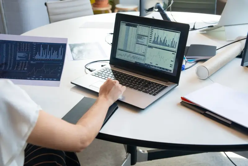 Laptop showing line charts beside a printed report on a round meeting table
