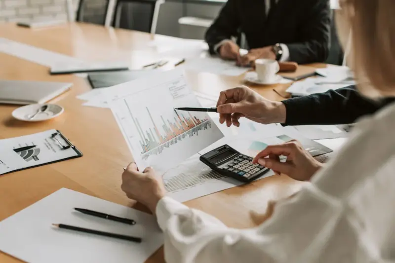 Team at a meeting table pointing at printed graphs with a calculator nearby