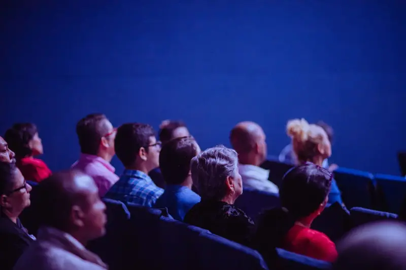 Rows of seated attendees watching a presentation in a dark blue auditorium