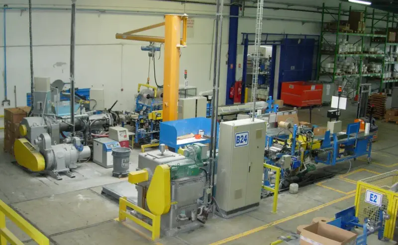 Row of plastic extruders with feed hoppers and barrels on a factory floor