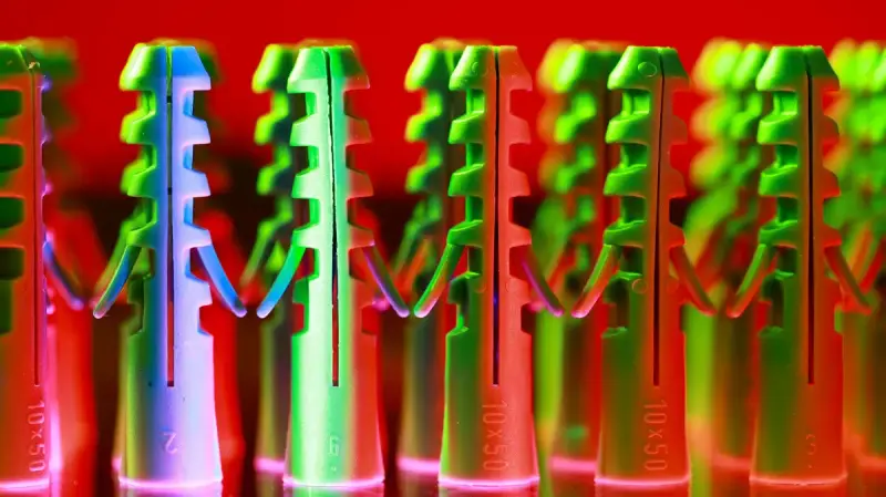 Rows of molded plastic wall anchors glowing green and red under colored light